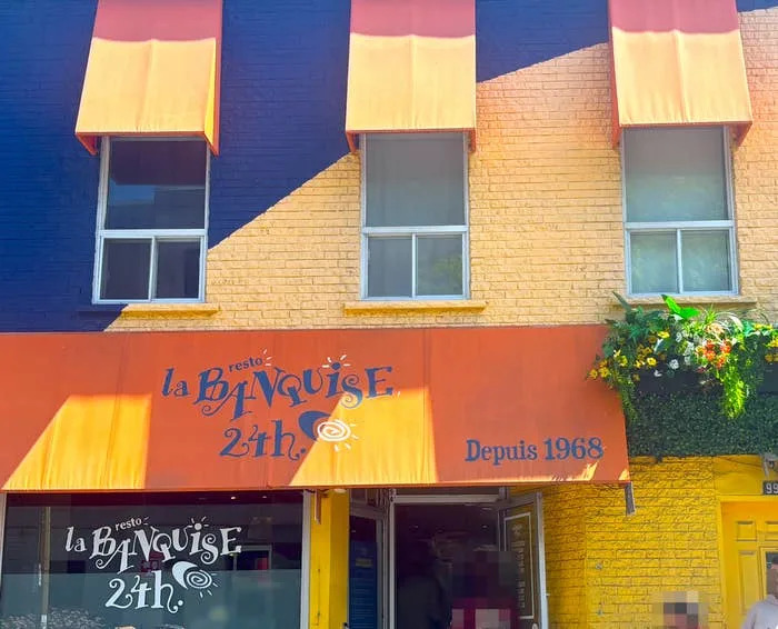 Exterior of La Banquise restaurant with striped awnings and floral decor, specializing in poutine since 1968