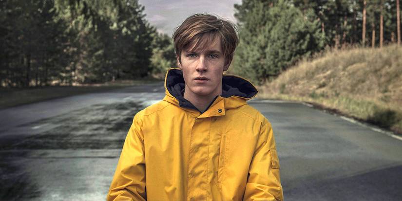 Jonas standing in the middle of a rural road with a raincoat on in the series Dark.