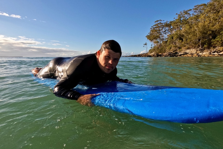 A man wearing a wetsuit lying on a surfboard in the ocean.