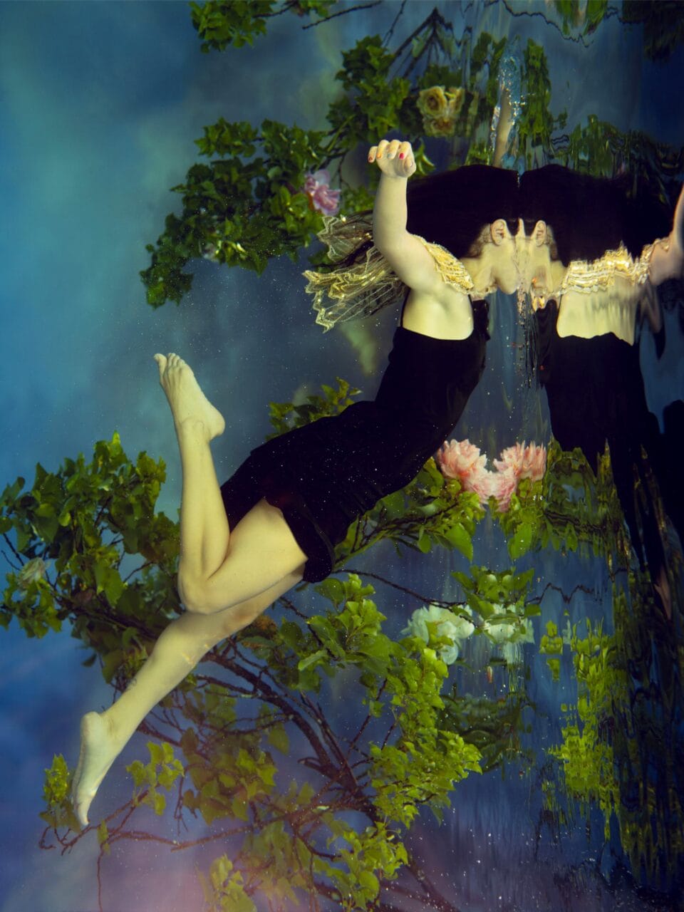 a photograph by Tamara Dean of a woman drifting in the water surrounded with trees and leaved, her face shrouded by ripples of water