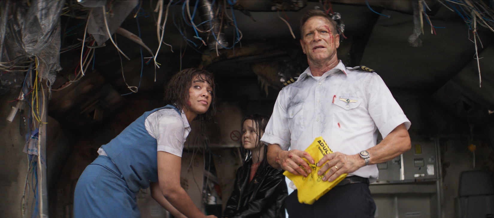 Survivors of a plane crash, led by a pilot played by Aaron Eckhart, stand in the remnants of their downed plane, looking out at the unseen ocean, in a scene from the shark thriller Deep Water