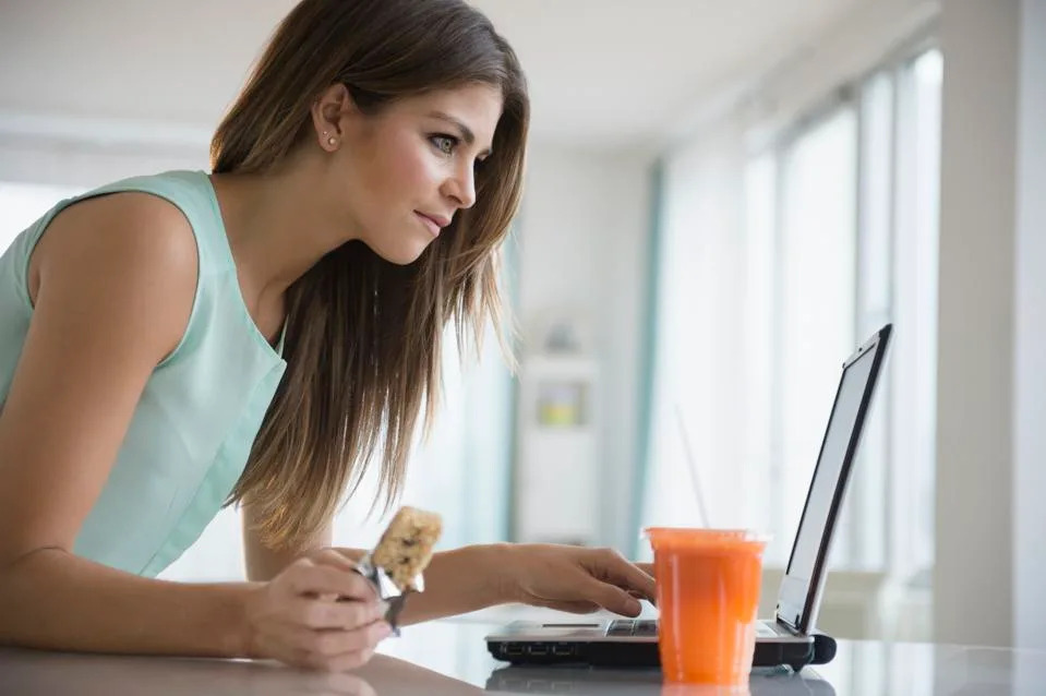 Young woman eating snack while working with laptop