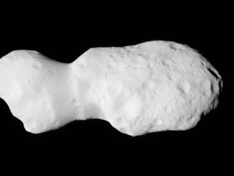 Asteroid wobbles in space: Closeup image of a potato-shaped rock with a narrow waist, covered with craters.