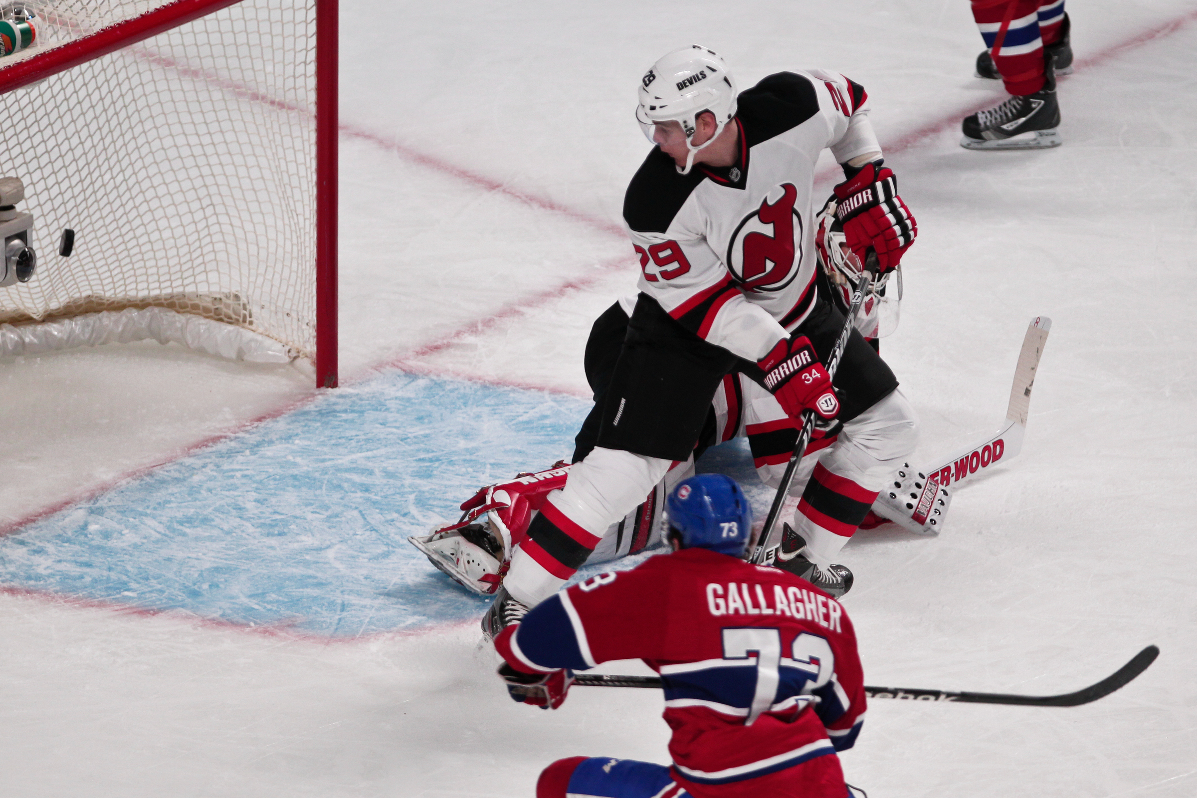 Brendan Gallagher follows through on a shot while a Devils goalie looks behind him at a puck in the net.