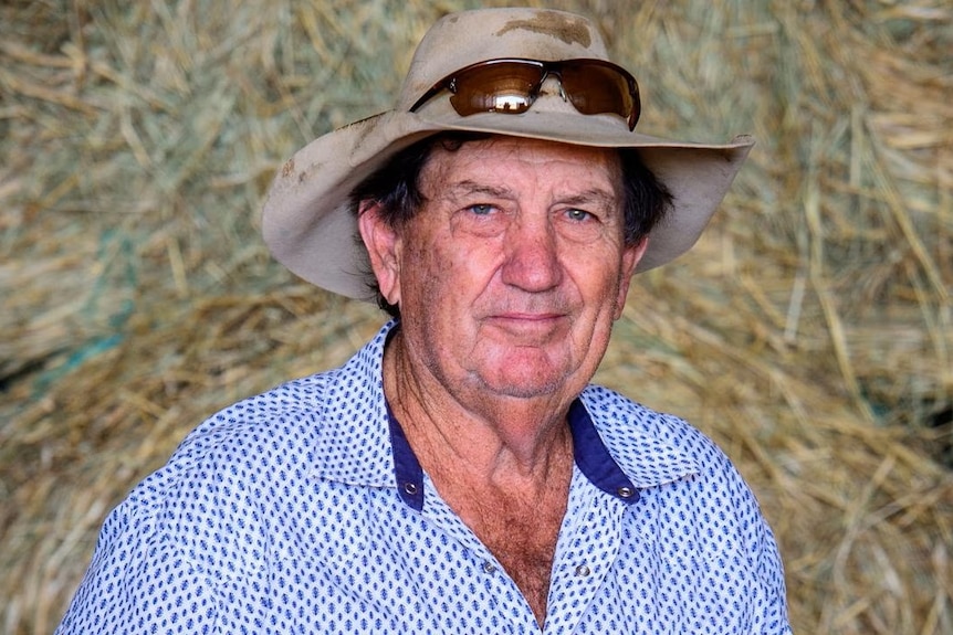 Richmond Shire mayor John Wharton smiles wearing a hat and shirt standing in front of hay bales.