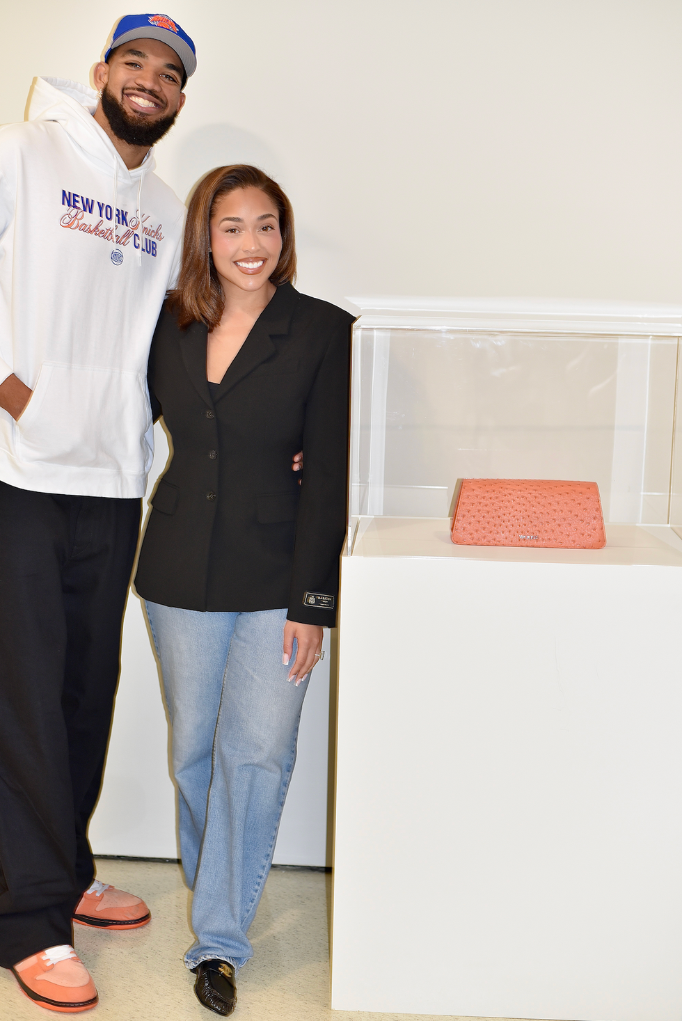 Two people posing in front of a display case with a coral handbag inside. Two people posing in front of a display case with a coral handbag inside.