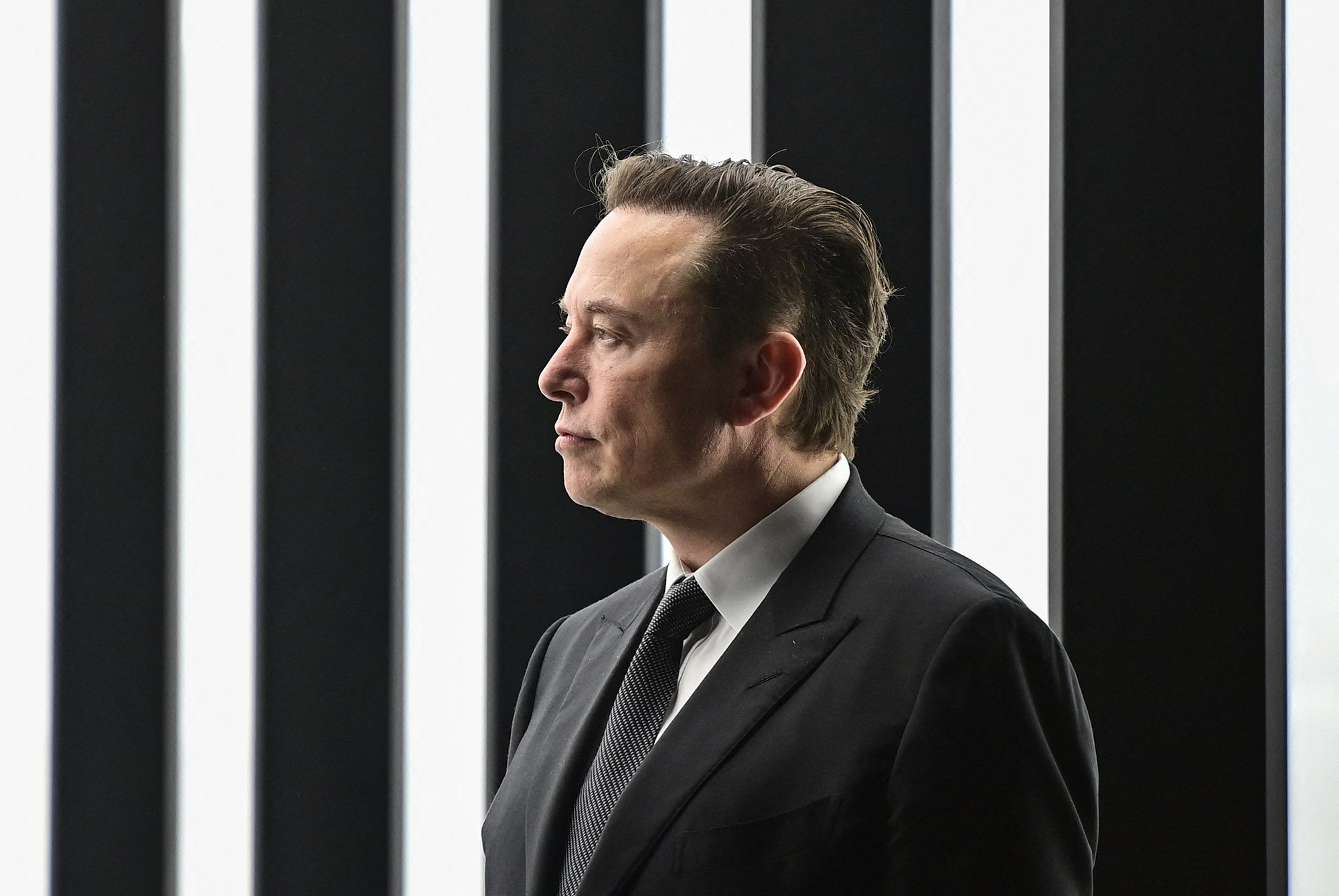 Elon Musk stands looking to his right.