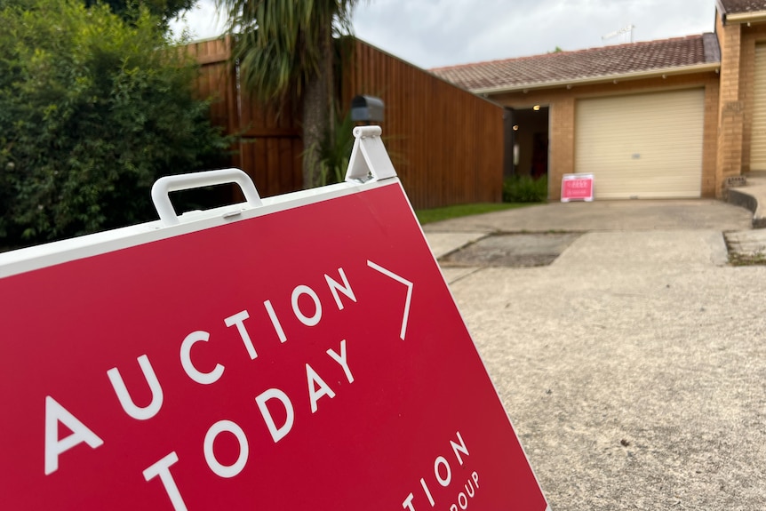 An A-frame sign that reads "auction today", directing towards a house.