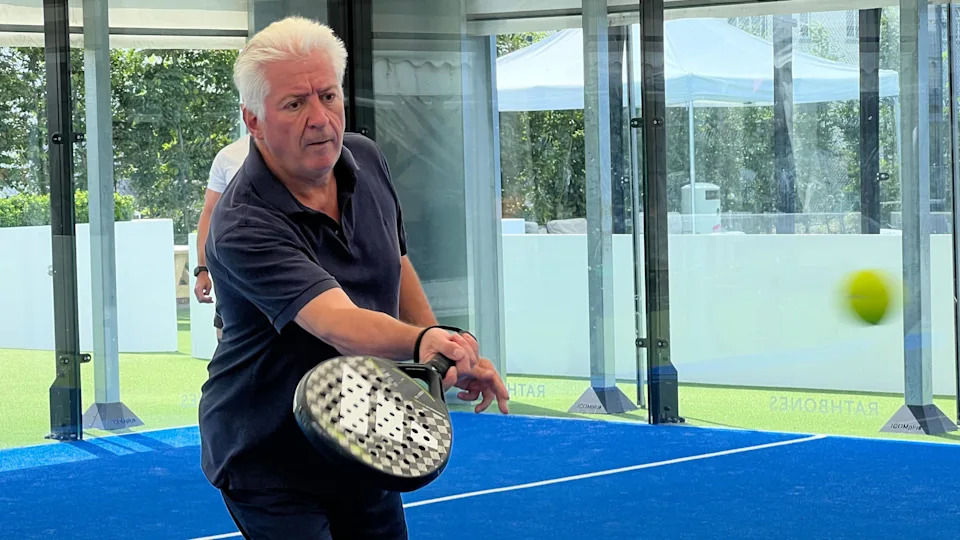 A man hits a ball with a padel racquet.