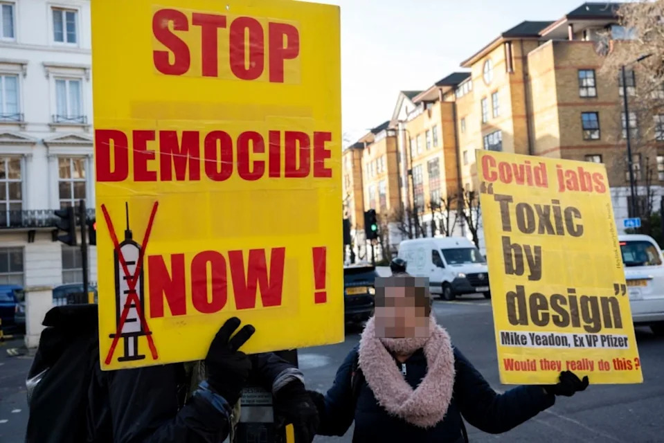 People holding signs at a protest. Signs read: "Stop Democide Now!" and "Covid jabs Toxic by design. Mike Yeadon, Ex VP Pfizer. Would they really do this?"