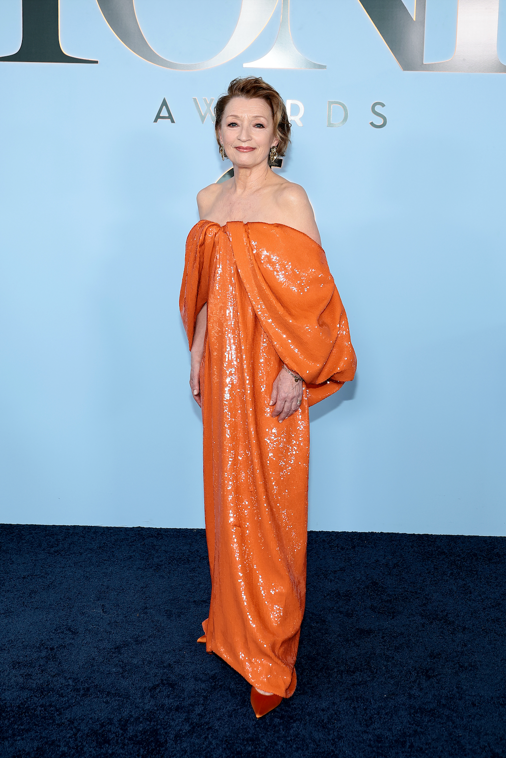Person wearing an orange, off-the-shoulder shimmering gown on a blue carpet.
