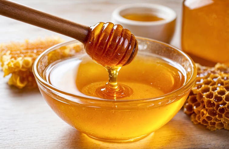A bowlful of honey, which a wooden spoon emerges from.
