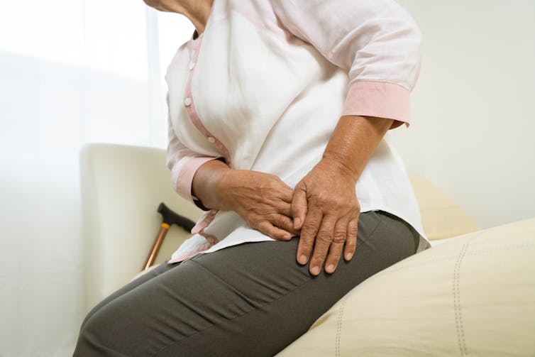 Senior person sitting on a bed holding onto their thigh and hip area as if in pain