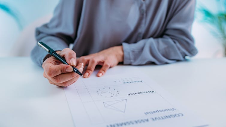 Cropped image of a person wearing a grey jumper completing a cognitive assessment on paper.