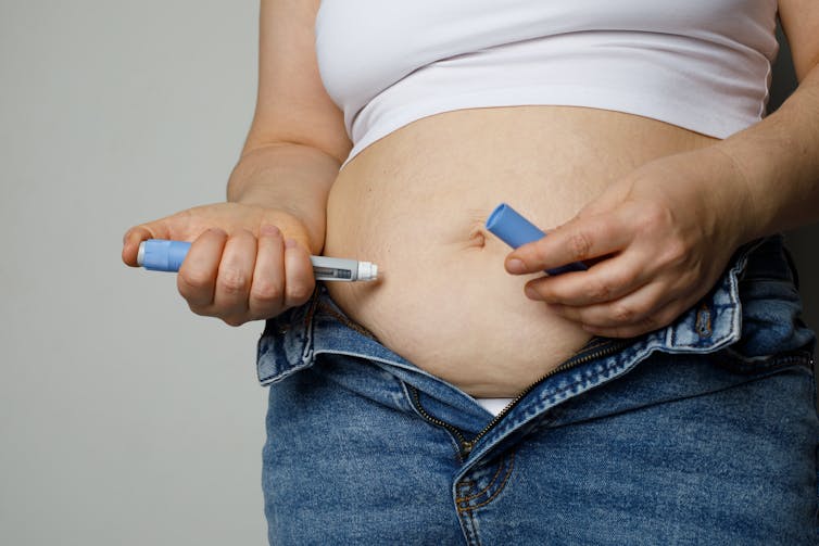 A photo of a woman injecting a weight loss jab pen into her abdomen.