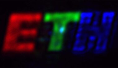 Blurry image showing the letters "ETH" with "E" in red, "T" in green, and "H" in blue, all against a black background.