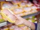 Woman choosing packed chicken meat in supermarket.