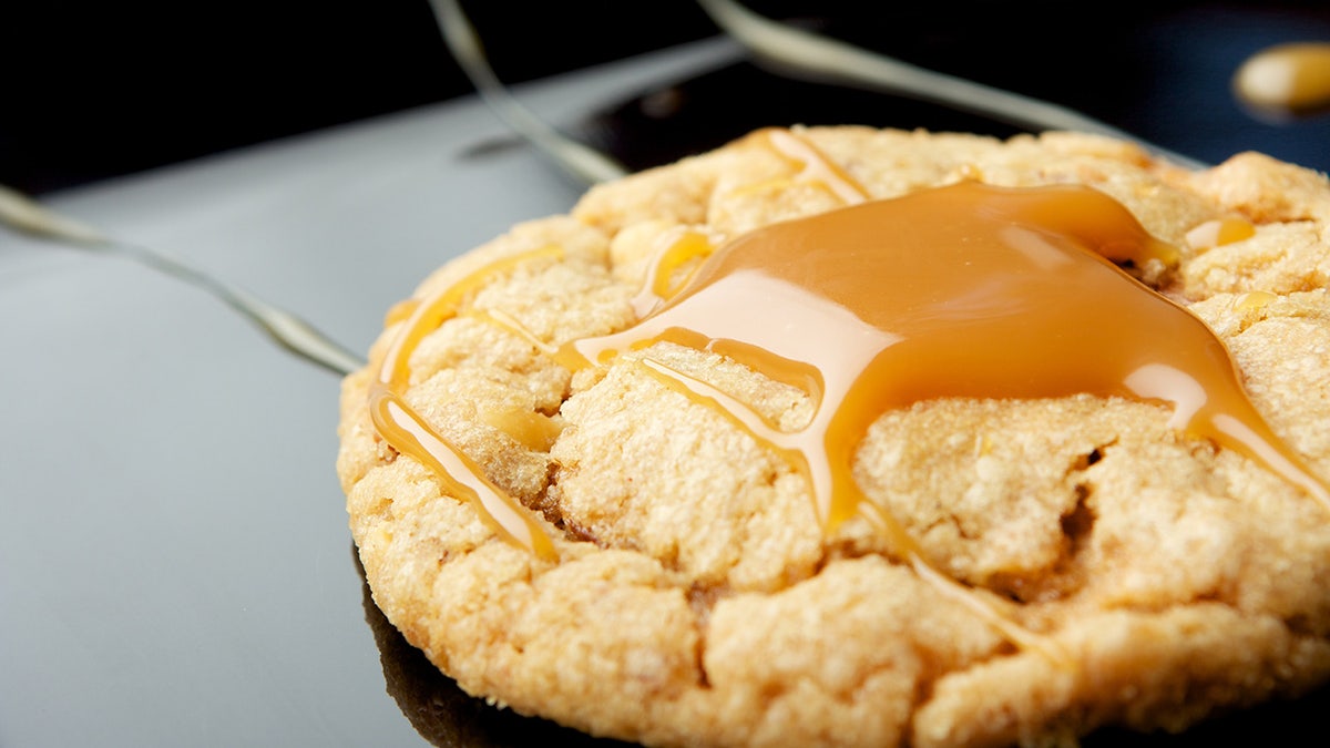 One peanut butter cookie with caramel drizzled on top on a white background