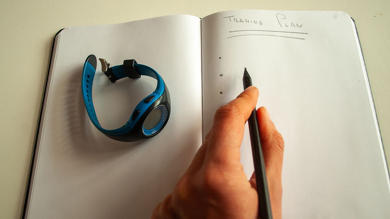 A person's hand writing in a journal with a fitness tracker next to them