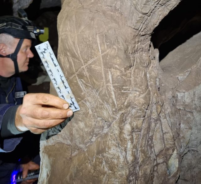 Moments after discovery, Lee Berger holds a photographic scale next to a crosshatched engraving