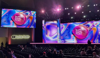 A view of a theater with folded chairs and a big stage with multiple screens set up.