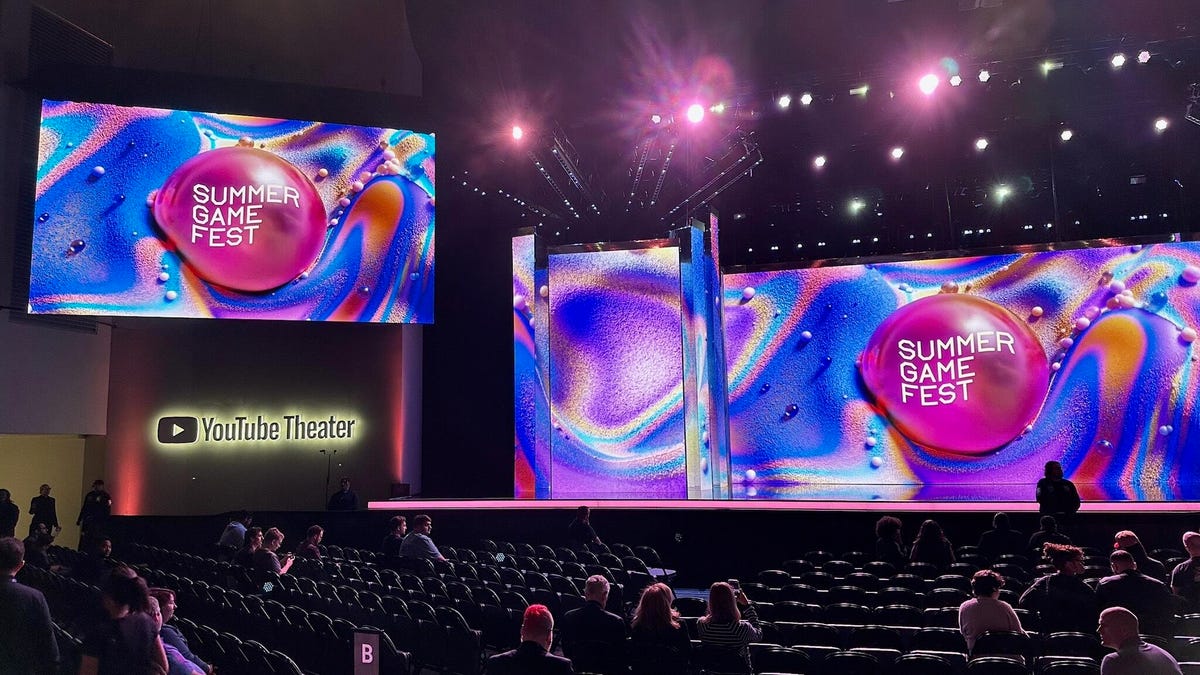 A view of a theater with folded chairs and a big stage with multiple screens set up.