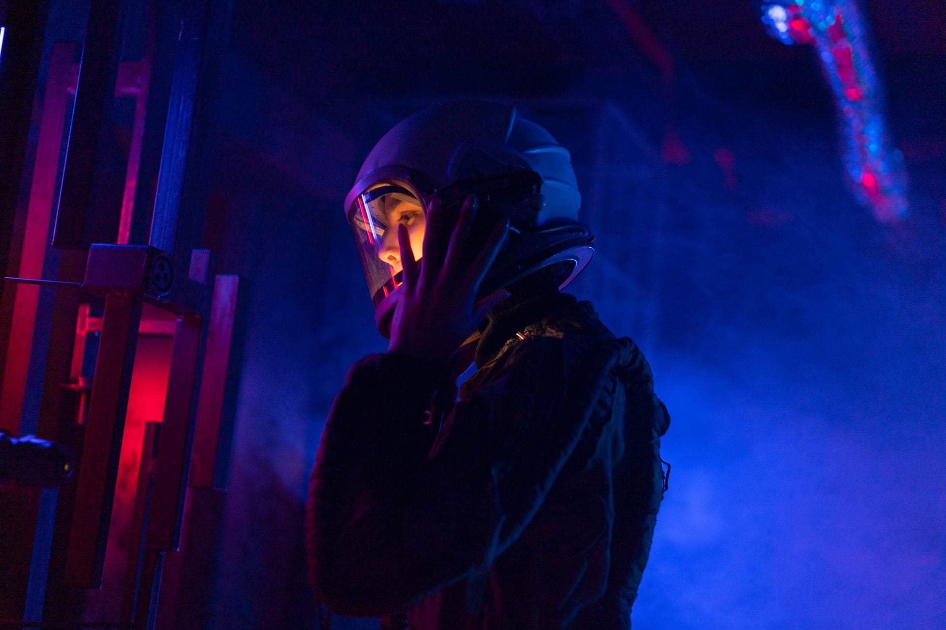 A female astronaut in a spacesuit explores a vividly lit, futuristic space setting.