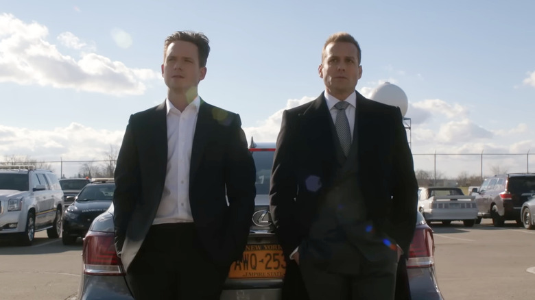 Mike Ross and Harvey Specter standing next to one another leaning on the trunk of a car