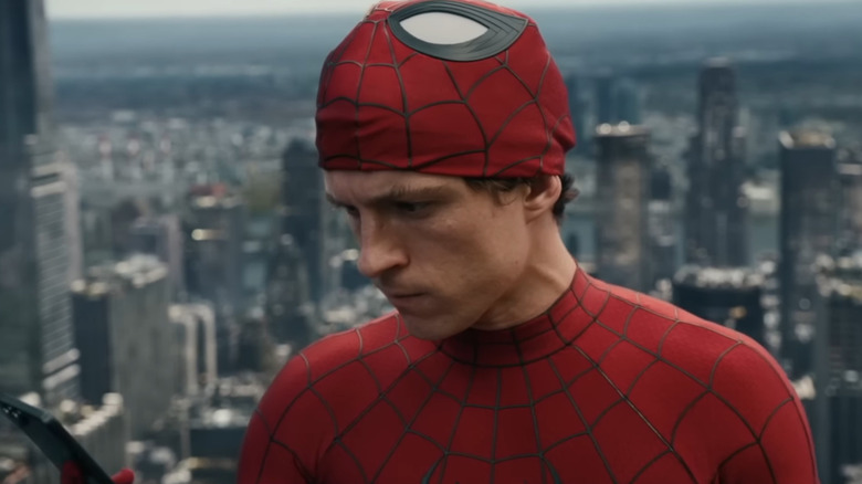 Tom Holland as Peter Parker wearing his Spider-Man outfit and looking at his phone from a tall skyscraper in Spider-Man: Brand New Day