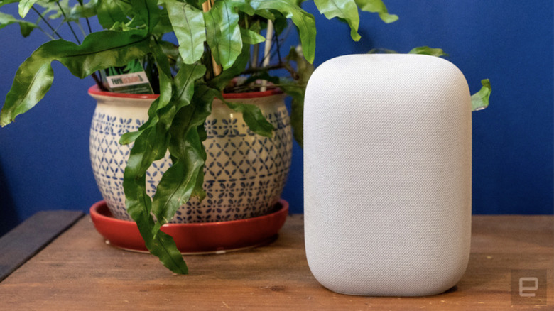 Photo of a Google Nest Audio speaker next to a houseplant in a large ceramic pot on a wooden table.