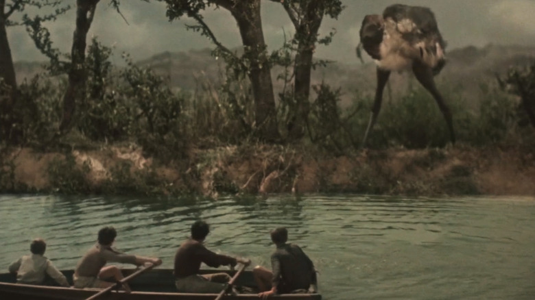 A boat full of boys looks at a giant dinosaur on the shore in Journey to the Beginning of Time