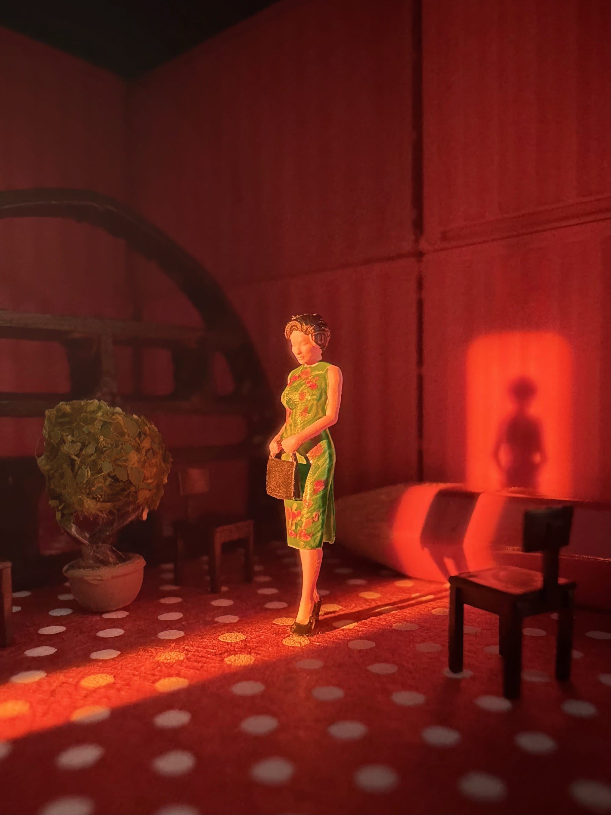 a photograph of a miniature tableau by Derrick Lin of a woman wearing a 1950s-era green dress, holding a handbag, and standing in red room