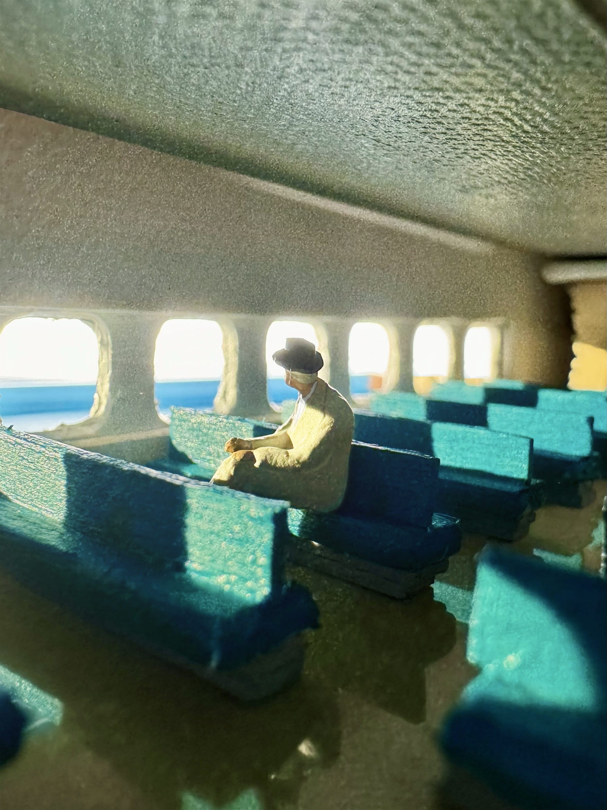 a photograph of a miniature tableau by Derrick Lin of a man in a fedora seated in an empty ferry, looking out the window