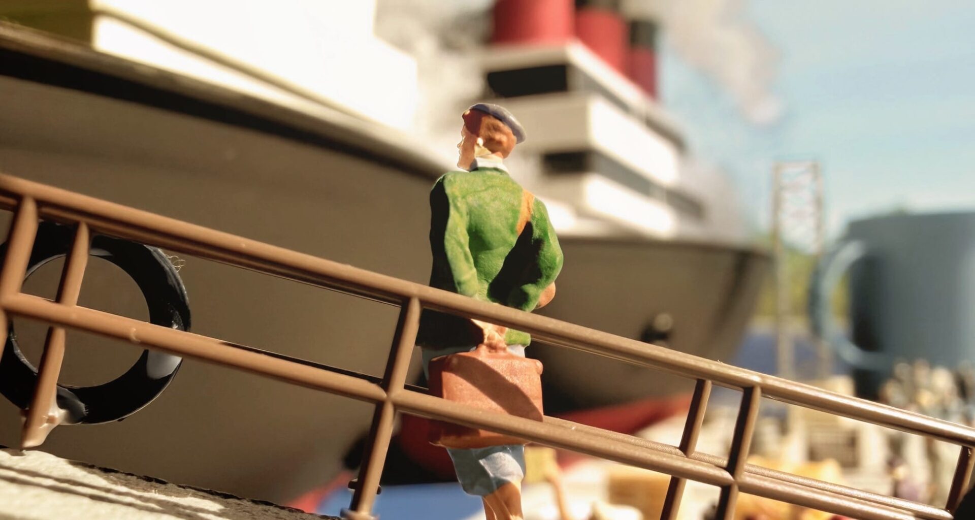 a photograph of a miniature tableau by Derrick Lin of a figure walking a gangplank onto a ship, carrying a small suitcase