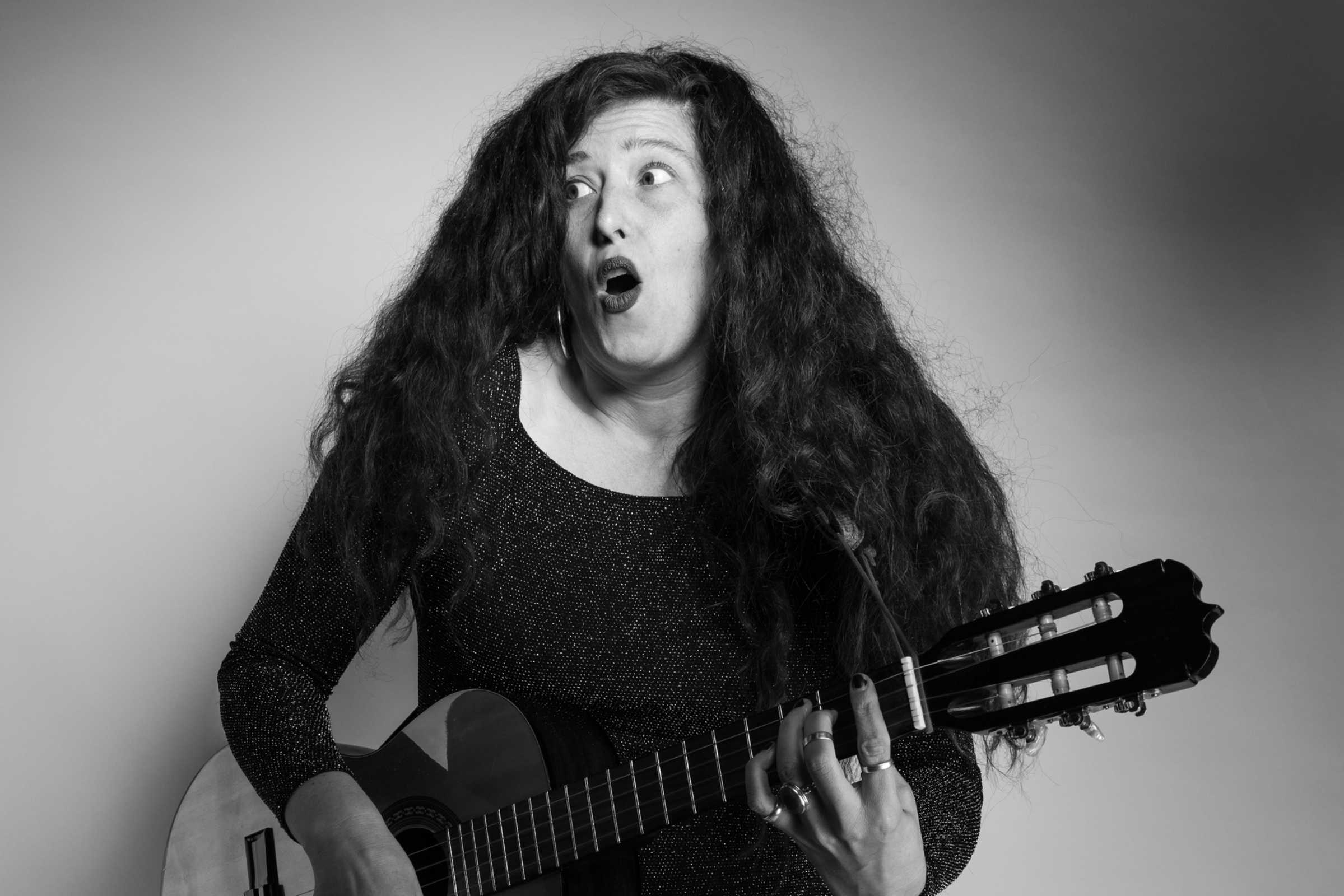 A woman holds a guitar in a black and white photo.
