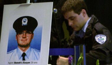 A police officer writes in a book, behind a photo of an officer on a placard with the words Agent Benoit L'Ecuyer, 29 ans