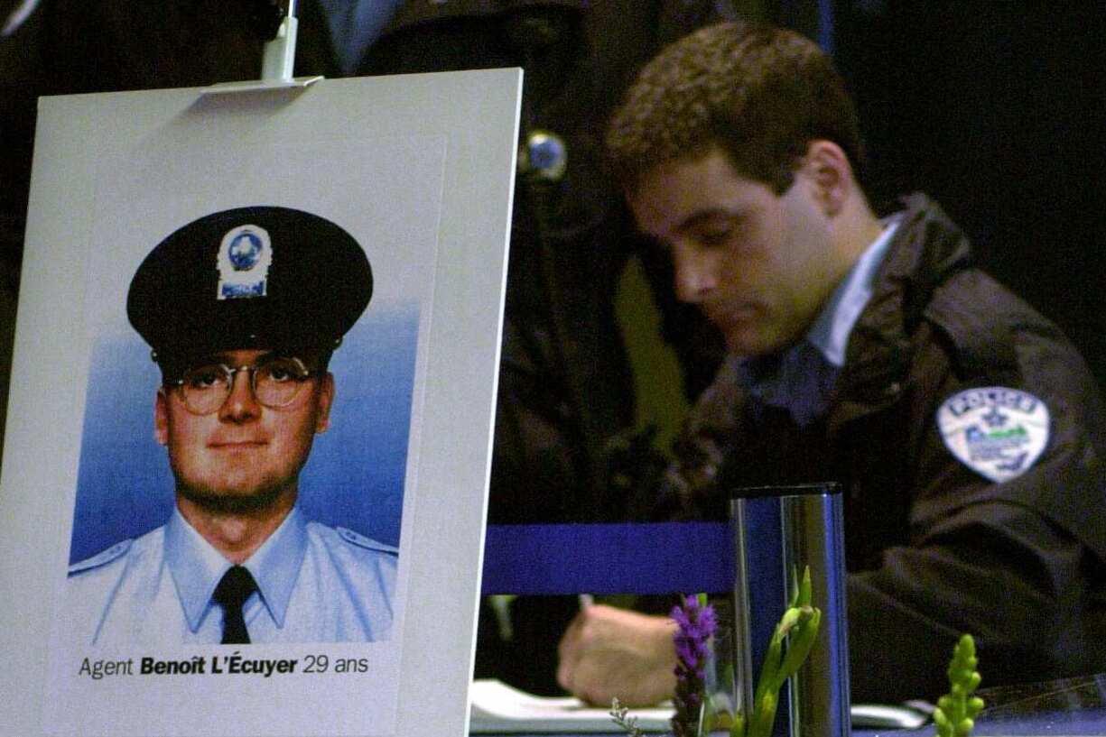 A police officer writes in a book, behind a photo of an officer on a placard with the words Agent Benoit L'Ecuyer, 29 ans