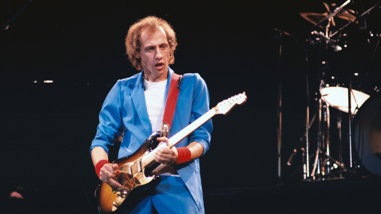 Mark Knopfler onstage with guitar in blue suit