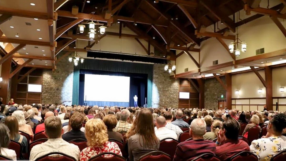 A room full of people sitting on chairs listening to a talk during a convention.