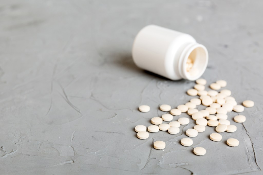 White pills spilled out of a white medicine bottle on a gray background.