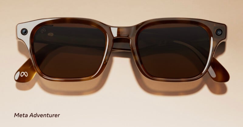 Brown rectangular sunglasses with dark lenses are displayed on a beige surface. Small cameras are embedded at the corners of the frame, and the Meta logo appears on the left temple tip. The text "Meta Adventurer" is shown below.