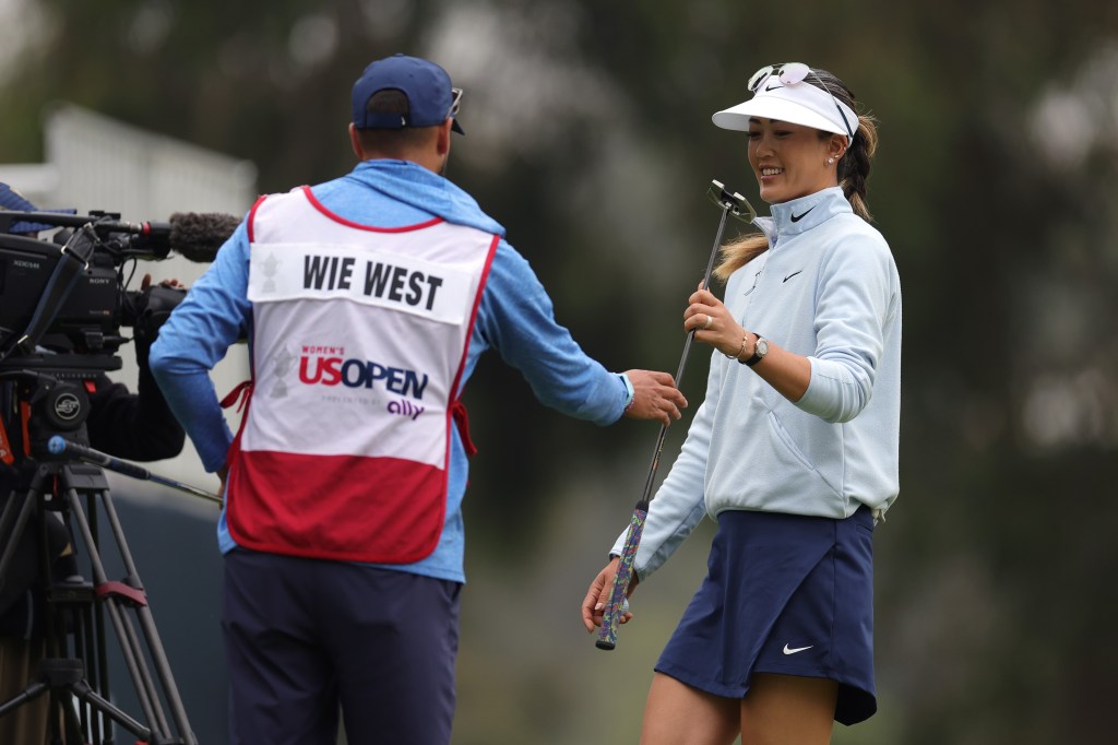 Michelle Wie West handing a club to caddie Jonnie West during a golf tournament.