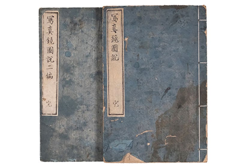 Two old blue Japanese books with vertical white labels and black text on the covers, showing signs of wear and traditional binding along the right edge.