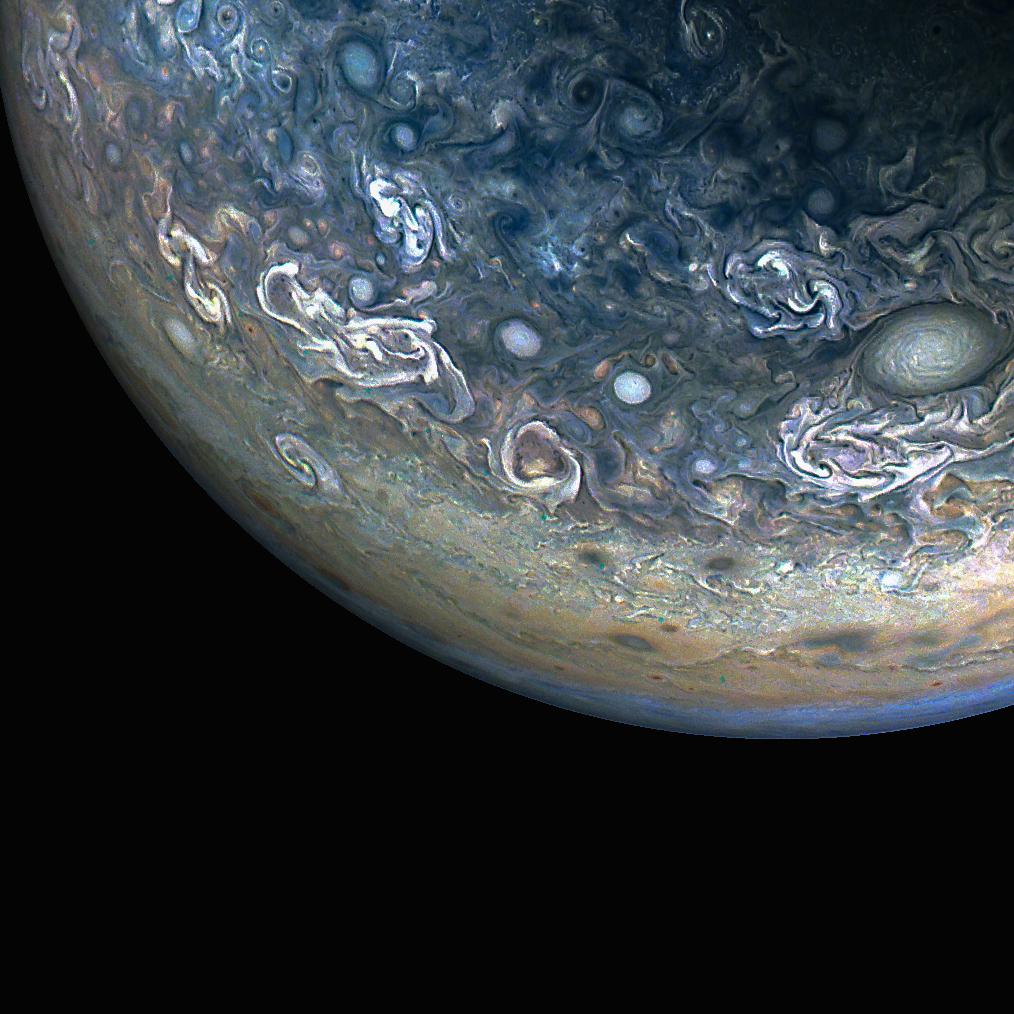 Three quarters of Jupiter can be seen in this photo; the darkness of space covers the bottom of the image. Green and blue swirls cover the planet's surface.
