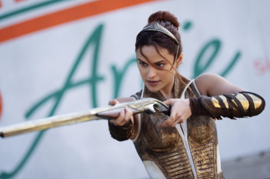 A woman wearing a crown and bronze armor points a rifle.