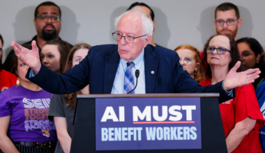 Bernie Sanders talking to a group of people with a podium saying "AI must benefit workers"