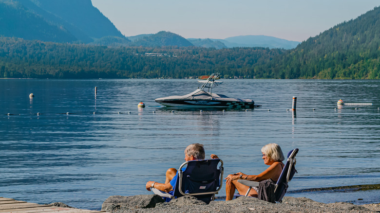 An elderly couple relaxing in beach chairs looking at a lake and mountains