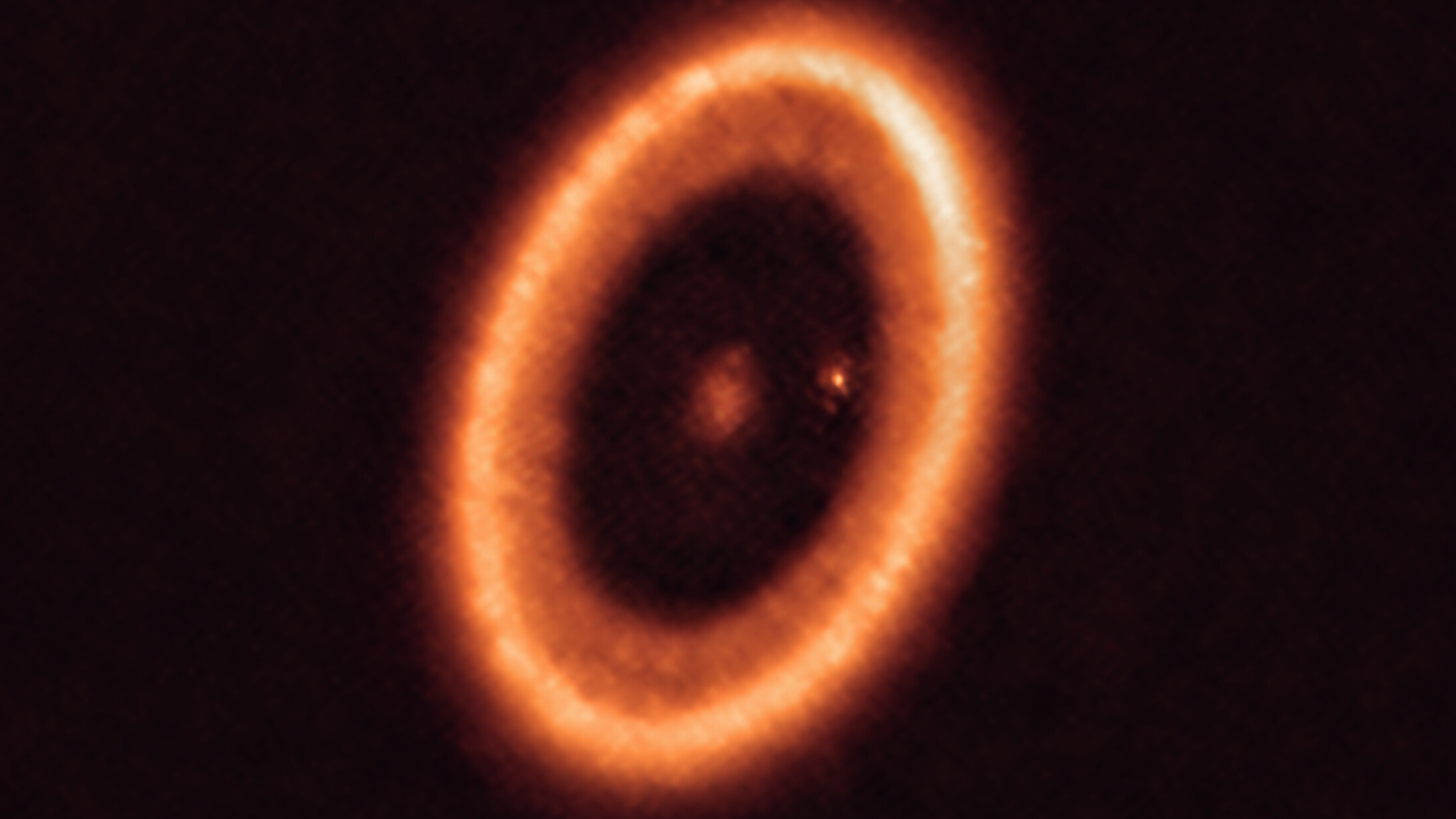 A hazy orange ring is seen in this image against a black background. A reddish dot in the center of the ring.