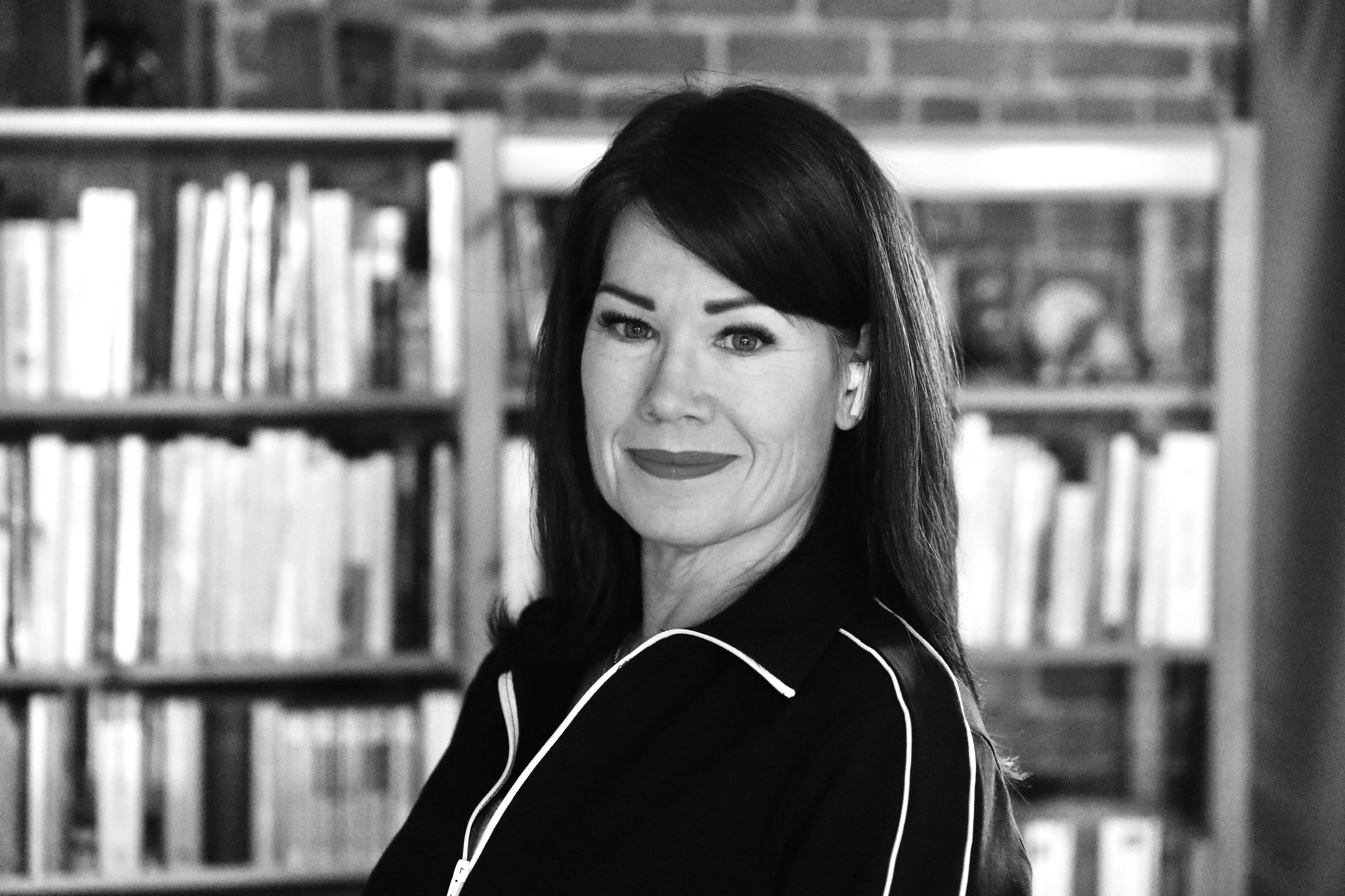 Profile photo of a woman in black and white. There are out-of-focus bookshelves in the background.