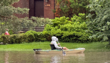 Man paddles a canoe in floodwaters outside a home.